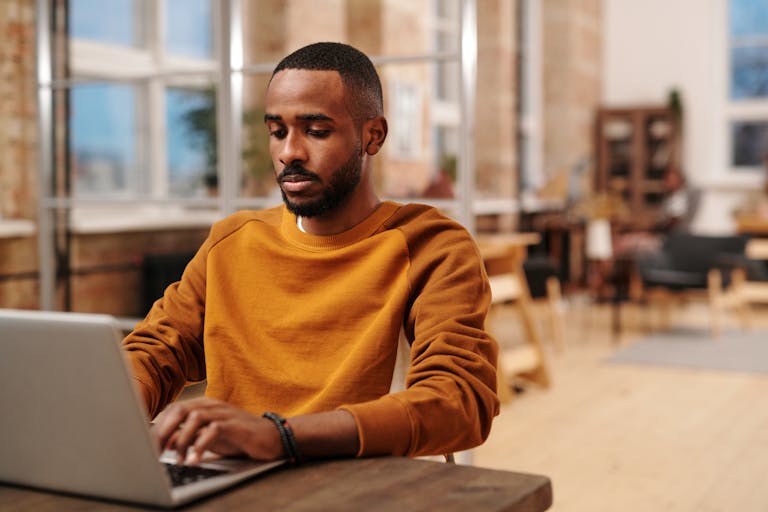 A focused man in a sweater working on his laptop in a modern office setting. Perfect for business and technology themes.