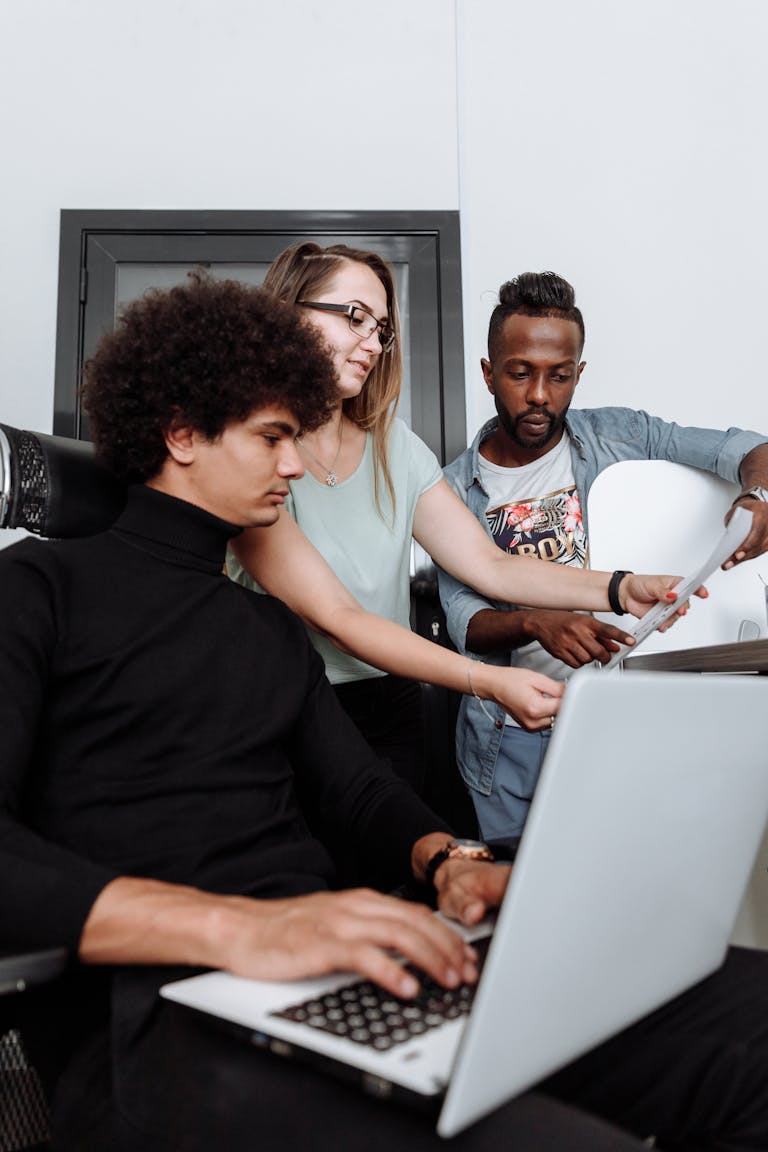 Three young adults collaborating on a project in a modern office environment.