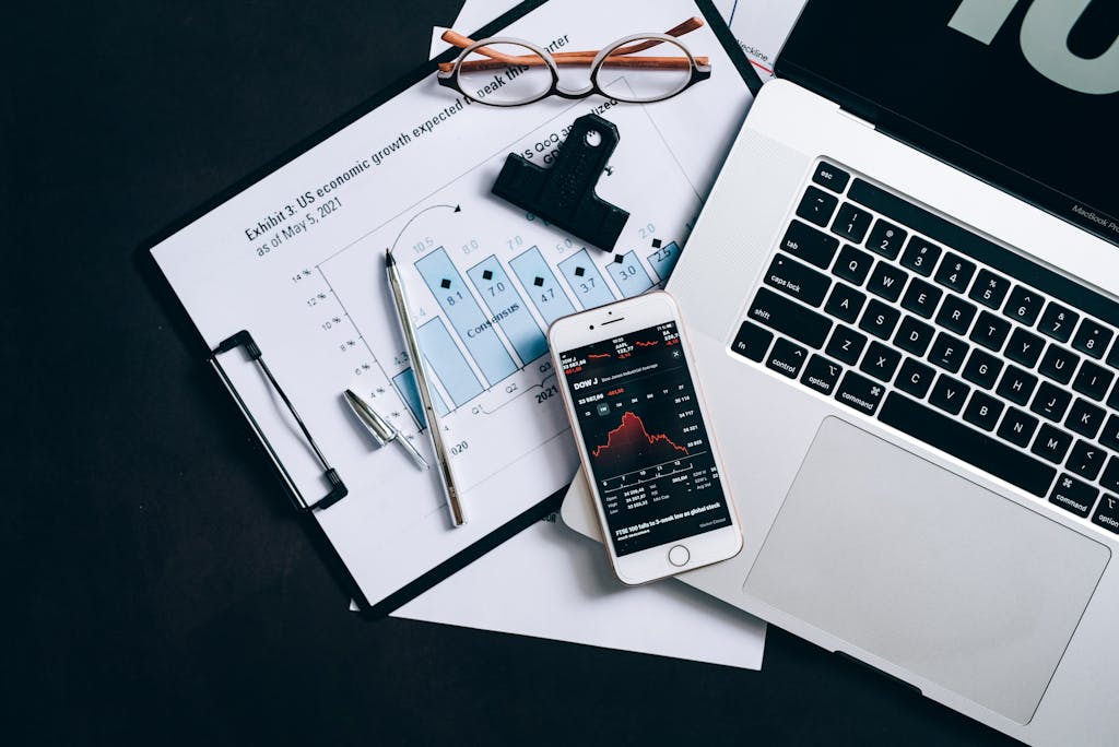 Top view of financial documents, laptop, and smartphone displaying stock market data.