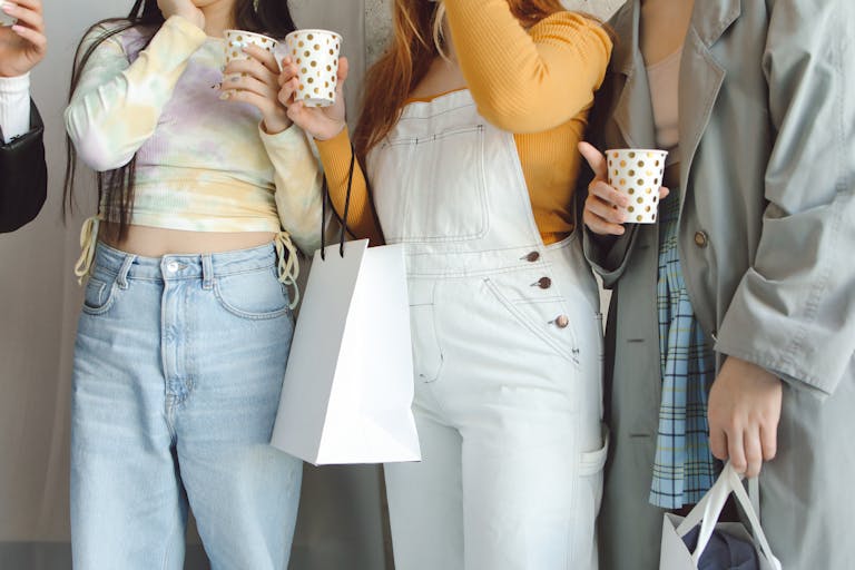 Young adults in fashionable outfits holding drinks and shopping bags, enjoying a casual gathering.