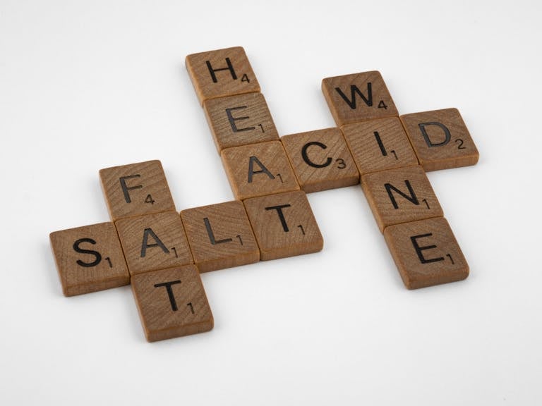 Wooden letter tiles arranged on a white surface creating a crossword with words like salt, fat, and wine.