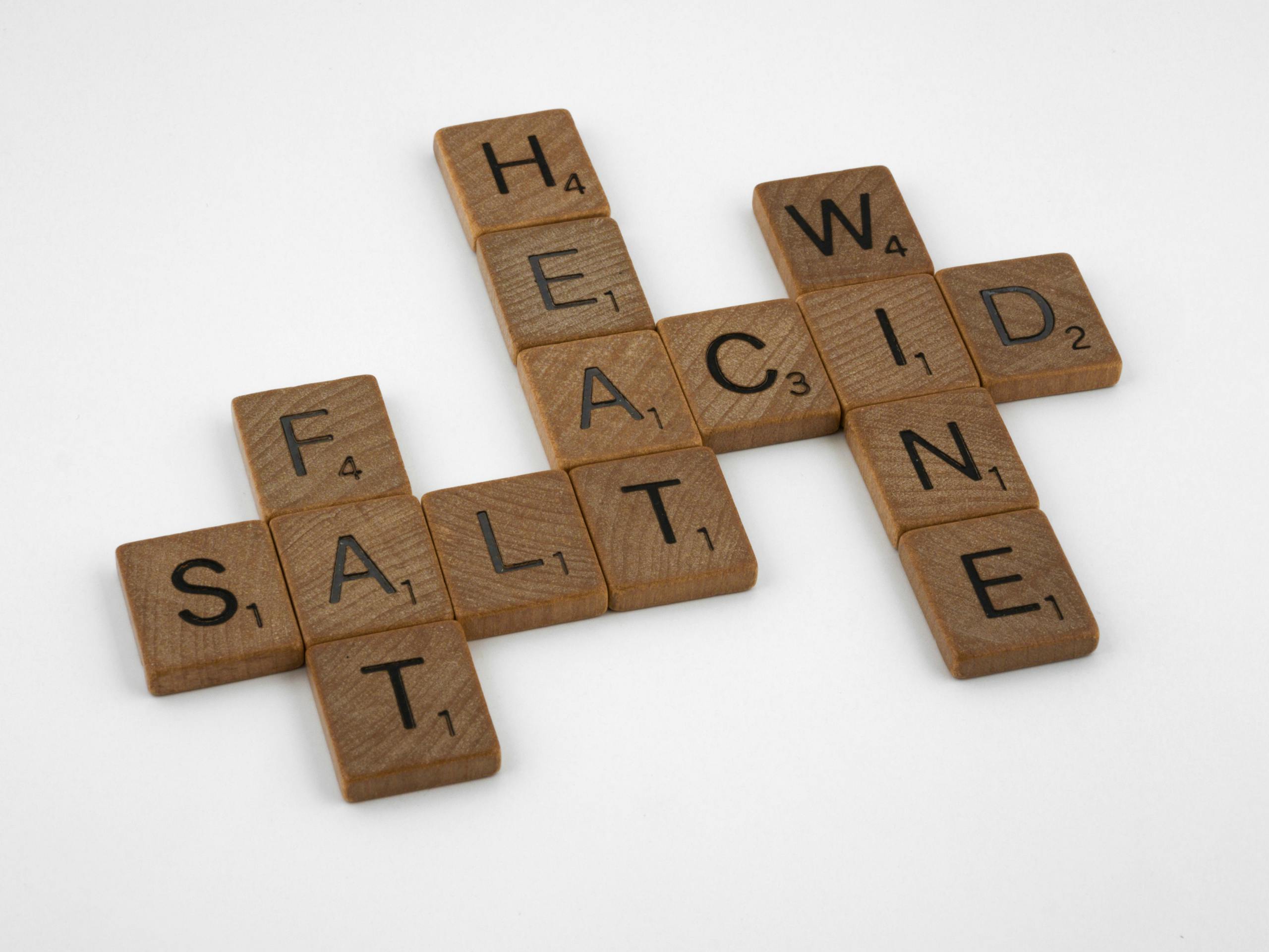Wooden letter tiles arranged on a white surface creating a crossword with words like salt, fat, and wine.